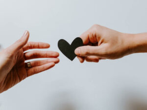 two hands passing a black paper heart