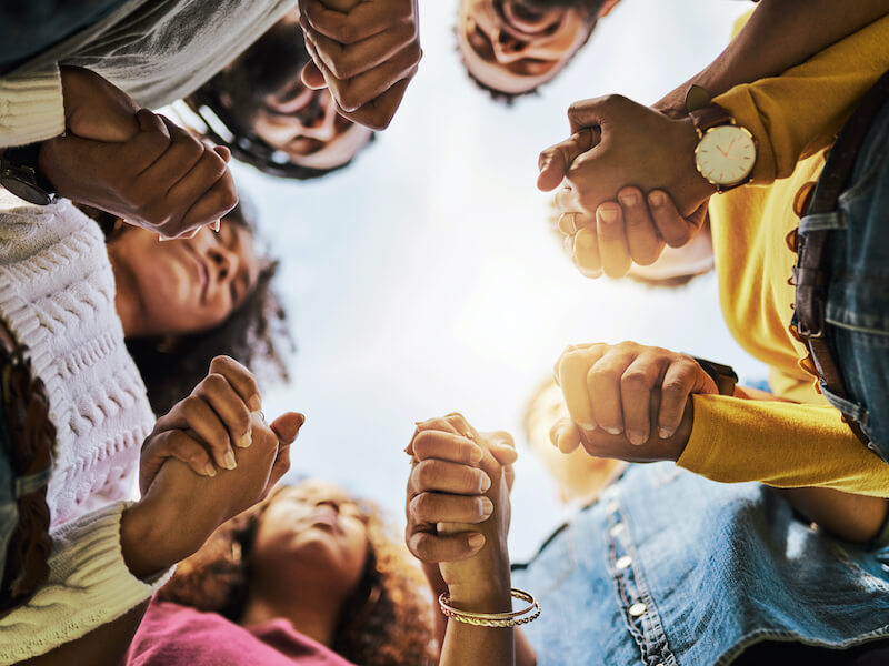 photo of a group of friends holding hand in a circle looking up from below hands