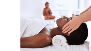 Beautiful young woman receives a head massage from a masseuse. A statue of Buddha sits in the background.